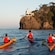 Three people kayaking on the water near a cliff in Portofino, Italy
